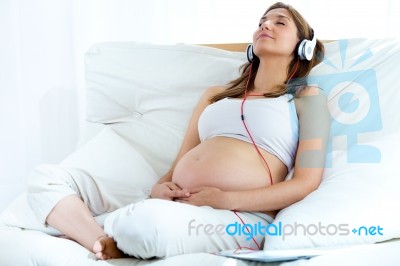 Pregnant Woman Sitting On Sofa At Home And Listening Music In He… Stock Photo