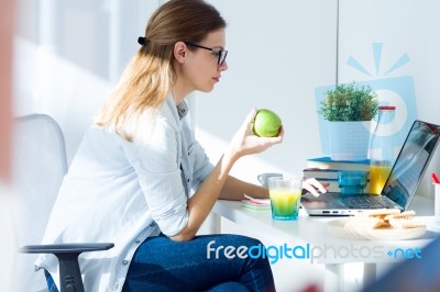 Pretty Young Woman Eating An Apple And Working At Home Stock Photo