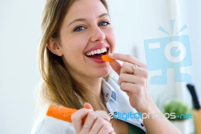 Pretty Young Woman Eating Carrot In The Kitchen Stock Photo