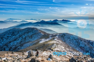 Professional Photographer Takes Photos With Camera On Tripod On Rocky Peak At Sunset Stock Photo