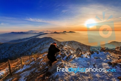 Professional Photographer Takes Photos With Camera On Tripod On Rocky Peak At Sunset Stock Photo