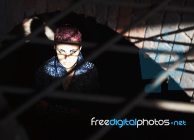 Punk Girl Sitting On The Floor Behind Metal Bars Stock Photo