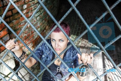 Punk Girl Sitting On The Floor Behind Metal Bars Stock Photo