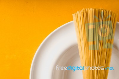 Raw Spaghetti  On The White Plate On The Yellow Background Stock Photo