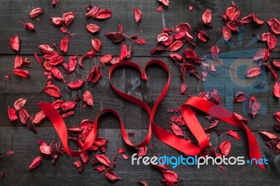 Red Bow Surrounded By Dried Petals On Wooden Background Stock Photo