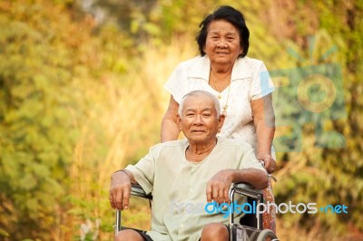 Senior Woman Pushing Her Disabled Hasband On Wheelchair Stock Photo