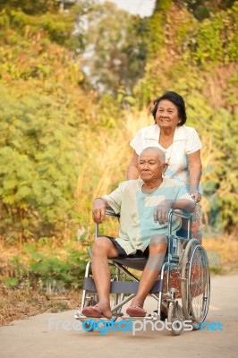 Senior Woman Pushing Her Disabled Hasband On Wheelchair Stock Photo