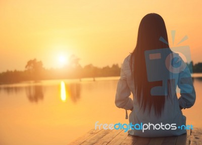 Silhouette Of Relaxing Young Woman On Wooden Pier At The Lake In Sunset Stock Photo