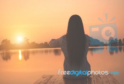 Silhouette Of Relaxing Young Woman On Wooden Pier At The Lake In Sunset Stock Photo