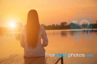 Silhouette Of Relaxing Young Woman On Wooden Pier At The Lake In Sunset Stock Photo