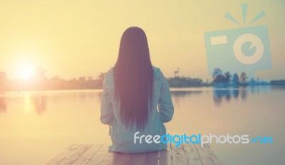 Silhouette Of Relaxing Young Woman On Wooden Pier At The Lake In Sunset Stock Photo