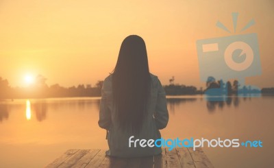 Silhouette Of Relaxing Young Woman On Wooden Pier At The Lake In Sunset Stock Photo