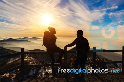 Silhouette Of Young Woman And Man With Backpacks And Sticks On Mountains At Sunset Stock Photo