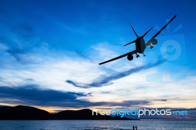 Silhouetted Commercial Airplane Flying Above The Sea At Sunset Stock Photo