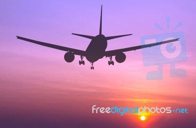 Silhouetted Commercial Airplane Flying At Sunset Stock Photo