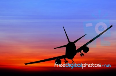 Silhouetted Commercial Airplane Flying At Sunset Stock Photo