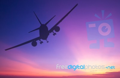 Silhouetted Commercial Airplane Flying At Sunset Stock Photo