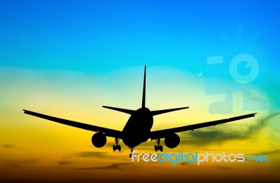 Silhouetted Commercial Airplane Flying At Sunset Stock Photo