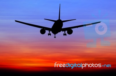 Silhouetted Commercial Airplane Flying At Sunset Stock Photo