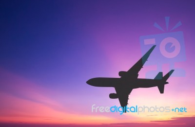 Silhouetted Commercial Airplane Flying At Sunset Stock Photo