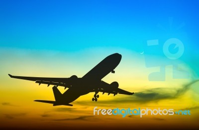 Silhouetted Commercial Airplane Flying At Sunset Stock Photo