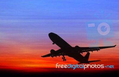 Silhouetted Commercial Airplane Flying At Sunset Stock Photo