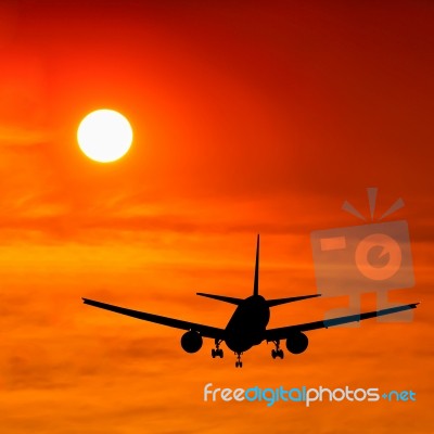 Silhouetted Commercial Airplane Flying At Sunset Stock Photo