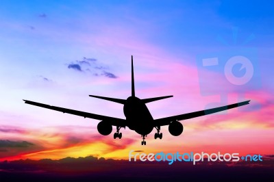 Silhouetted Commercial Airplane Flying At Sunset Stock Photo