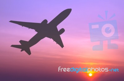 Silhouetted Commercial Airplane Flying At Sunset Stock Photo