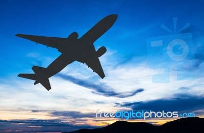 Silhouetted Commercial Airplane Flying At Sunset Stock Photo