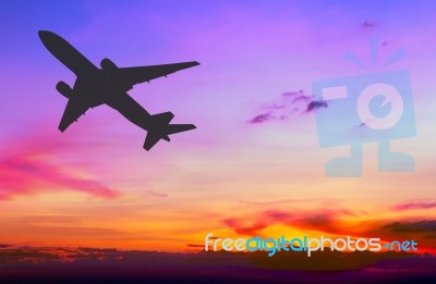 Silhouetted Commercial Airplane Flying At Sunset Stock Photo