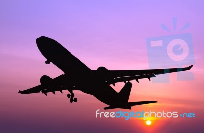 Silhouetted Commercial Airplane Flying At Sunset Stock Photo