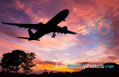 Silhouetted Commercial Airplane Flying At Sunset Stock Photo