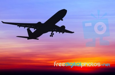 Silhouetted Commercial Airplane Flying At Sunset Stock Photo