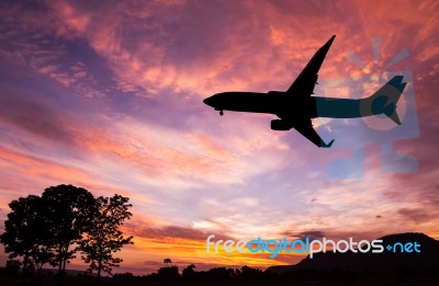 Silhouetted Commercial Airplane Flying At Sunset Stock Photo