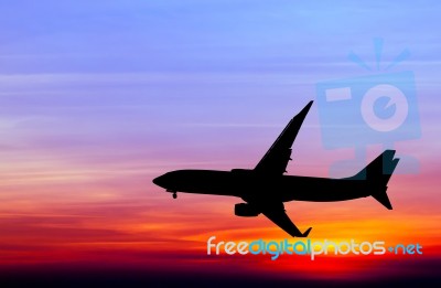 Silhouetted Commercial Airplane Flying At Sunset Stock Photo