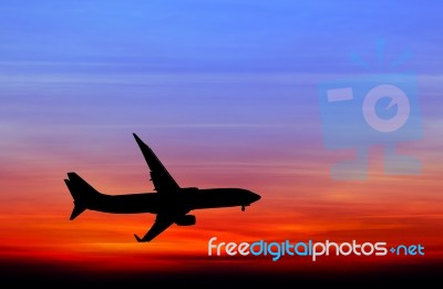 Silhouetted Commercial Airplane Flying At Sunset Stock Photo