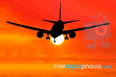 Silhouetted Commercial Airplane Flying At Sunset Stock Photo