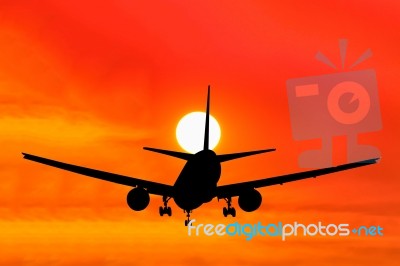 Silhouetted Commercial Airplane Flying At Sunset Stock Photo