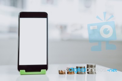 Smartphone Blank Screen Placed On A Vertical Green Stand, And The Coins Are Arranged In A Row. Represents The Growth Of Financial Stock Photo