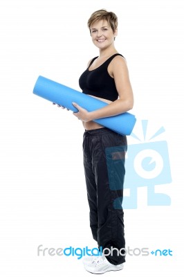 Smiling Female Instructor Carrying A Blue Yoga Mat Stock Photo