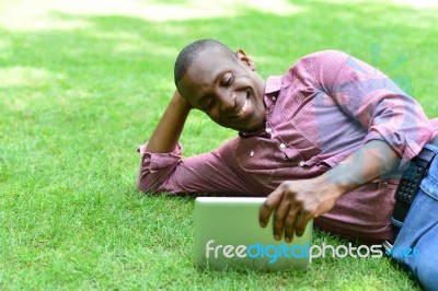 Smiling Man Lying On The Lawn With Tablet Stock Photo