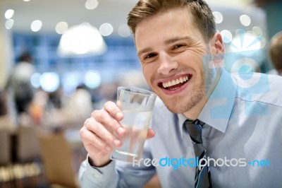 Smiling Young Man Drinking Water In Restaurant Stock Photo