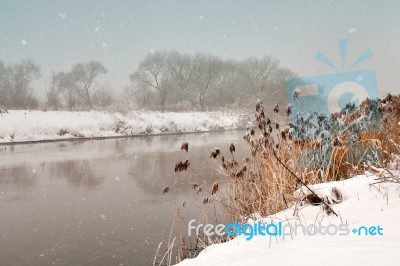 Snowfall Over The River. Winter Misty Cloudy Snowy Weather Stock Photo