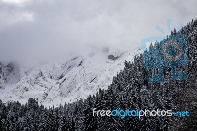 Snowy Mountain Range With Clouds And A Forest Stock Photo