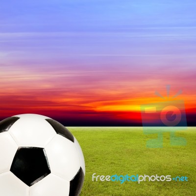 Soccer Ball With Green Grass Field Against Sunset Sky Stock Photo