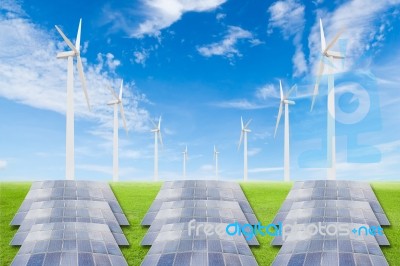 Solar Panels And Wind Turbine On Green Grass Field Against Blue Stock Photo