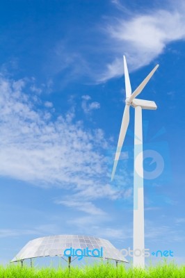 Solar Panels And Wind Turbine On Green Grass Field Against Blue Stock Photo