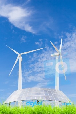 Solar Panels And Wind Turbine On Green Grass Field Against Blue Stock Photo