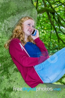 Teenage Girl In Tree Calling With Mobile Phone Stock Photo